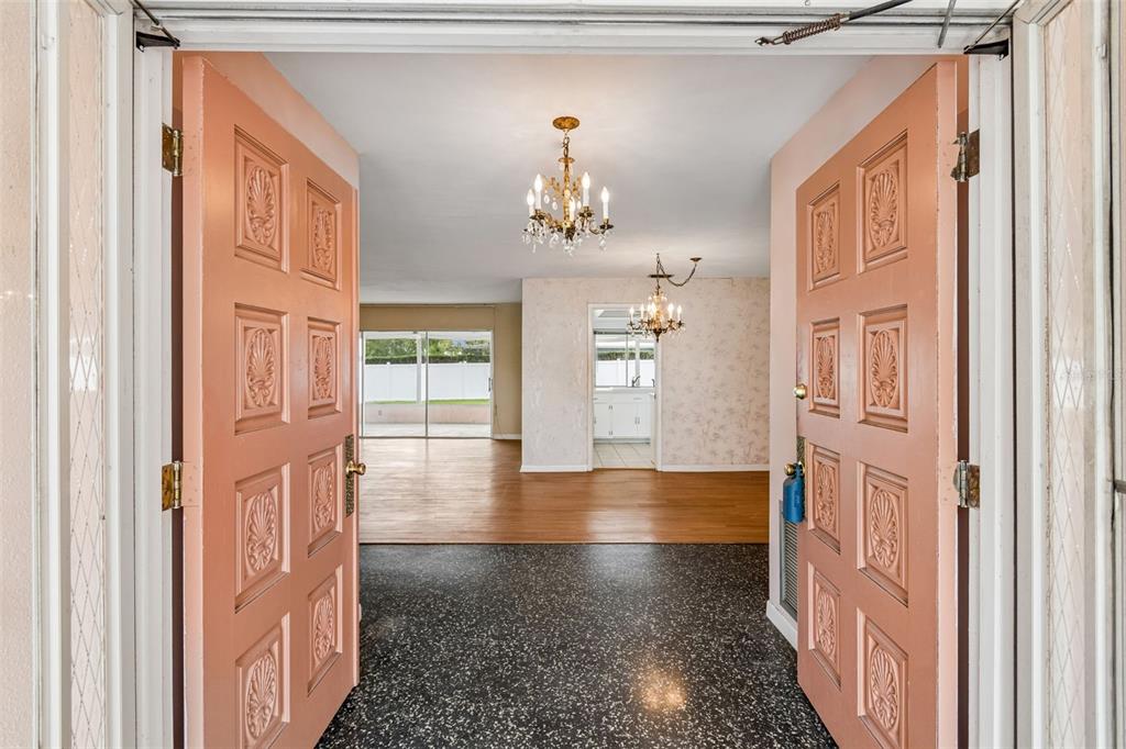 A view through open pink double doors into a foyer with terrazzo flooring and chandeliers — 14363 NEPTUNE ROAD, SEMINOLE, FL