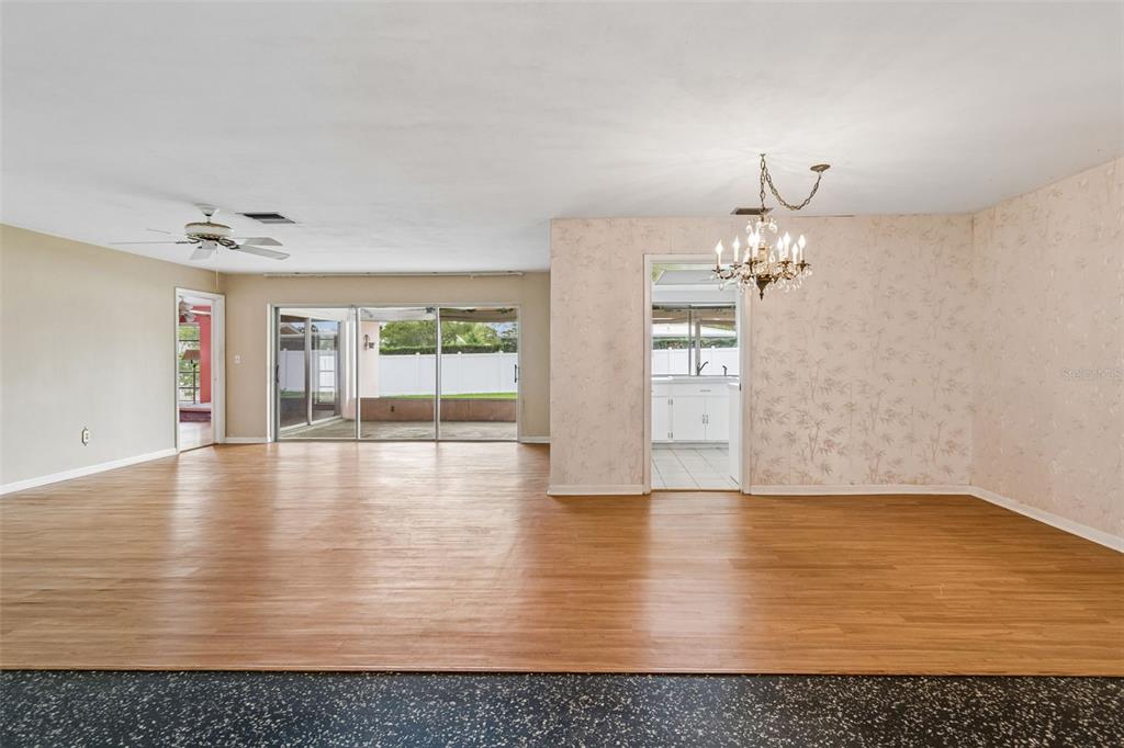 A living and dining area with wood-look flooring, wallpapered walls, and a crystal chandelier — 14363 NEPTUNE ROAD, SEMINOLE, FL