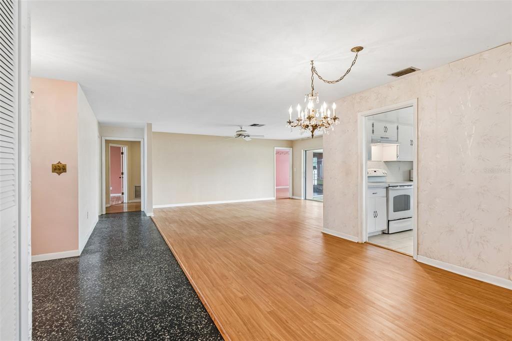An open-concept living and dining area features wood-look flooring, a chandelier, and a kitchen doorway — 14363 NEPTUNE ROAD, SEMINOLE, FL