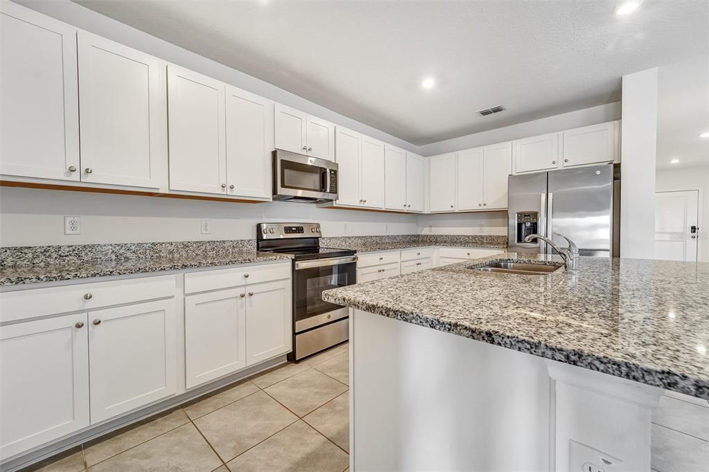 A kitchen features white cabinets, granite countertops, stainless steel appliances, and a central island — 6785 BRANHAM MILL COURT, ZEPHYRHILLS, FL