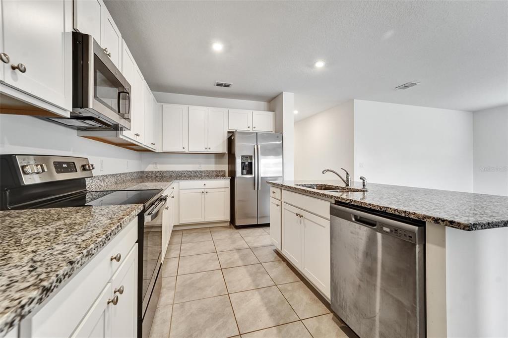 A kitchen features white cabinets, granite countertops, stainless steel appliances, and tile flooring — 6785 BRANHAM MILL COURT, ZEPHYRHILLS, FL