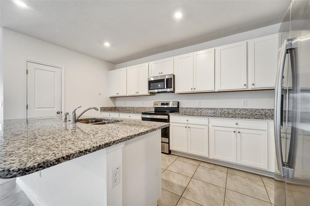 A kitchen features white cabinets, granite countertops, stainless steel appliances, and a central island — 6785 BRANHAM MILL COURT, ZEPHYRHILLS, FL