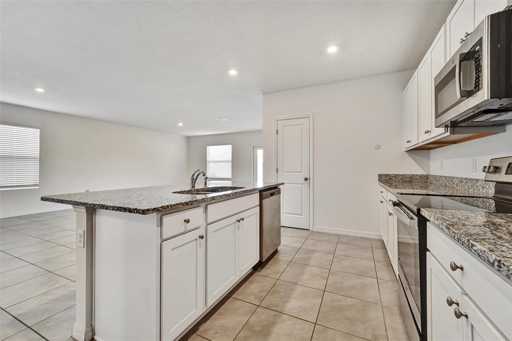 A kitchen features white cabinets, granite countertops, stainless steel appliances, and tile flooring — 6785 BRANHAM MILL COURT, ZEPHYRHILLS, FL