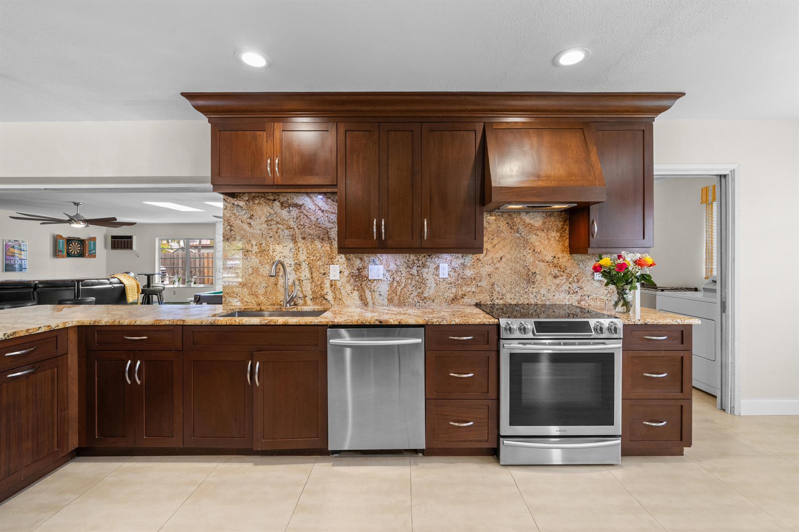 A kitchen features dark wood cabinets, granite countertops, a full-height backsplash, and stainless steel appliances — 1500 SE 24th Avenue, Pompano Beach FL 33062, POMPANO BEACH, FL