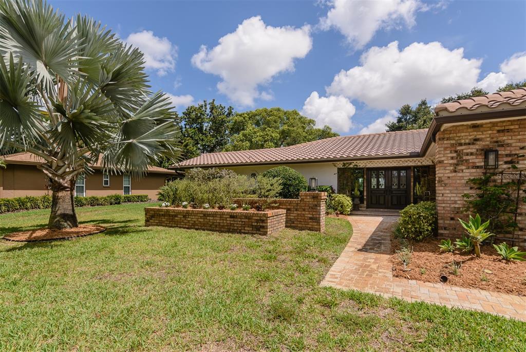 A brick-paved walkway leads to the front entrance of a single-story brick house — 2860 QUAIL HOLLOW ROAD W, CLEARWATER, FL