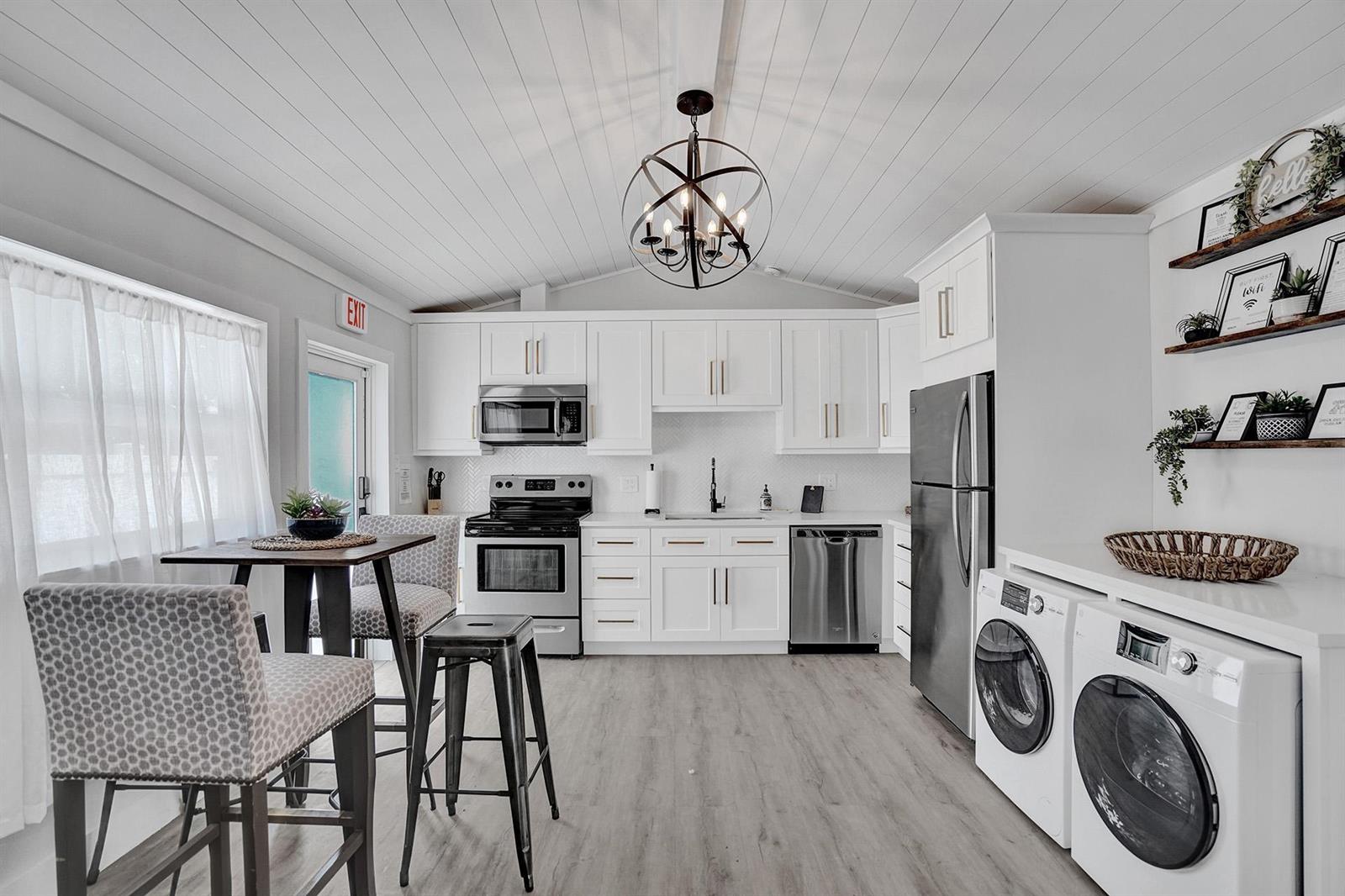 A kitchen with white cabinets, stainless steel appliances, a dining table, and laundry machines — 1969 NE 5th Street # 2, Deerfield Beach FL 33441, DEERFIELD BEACH, FL