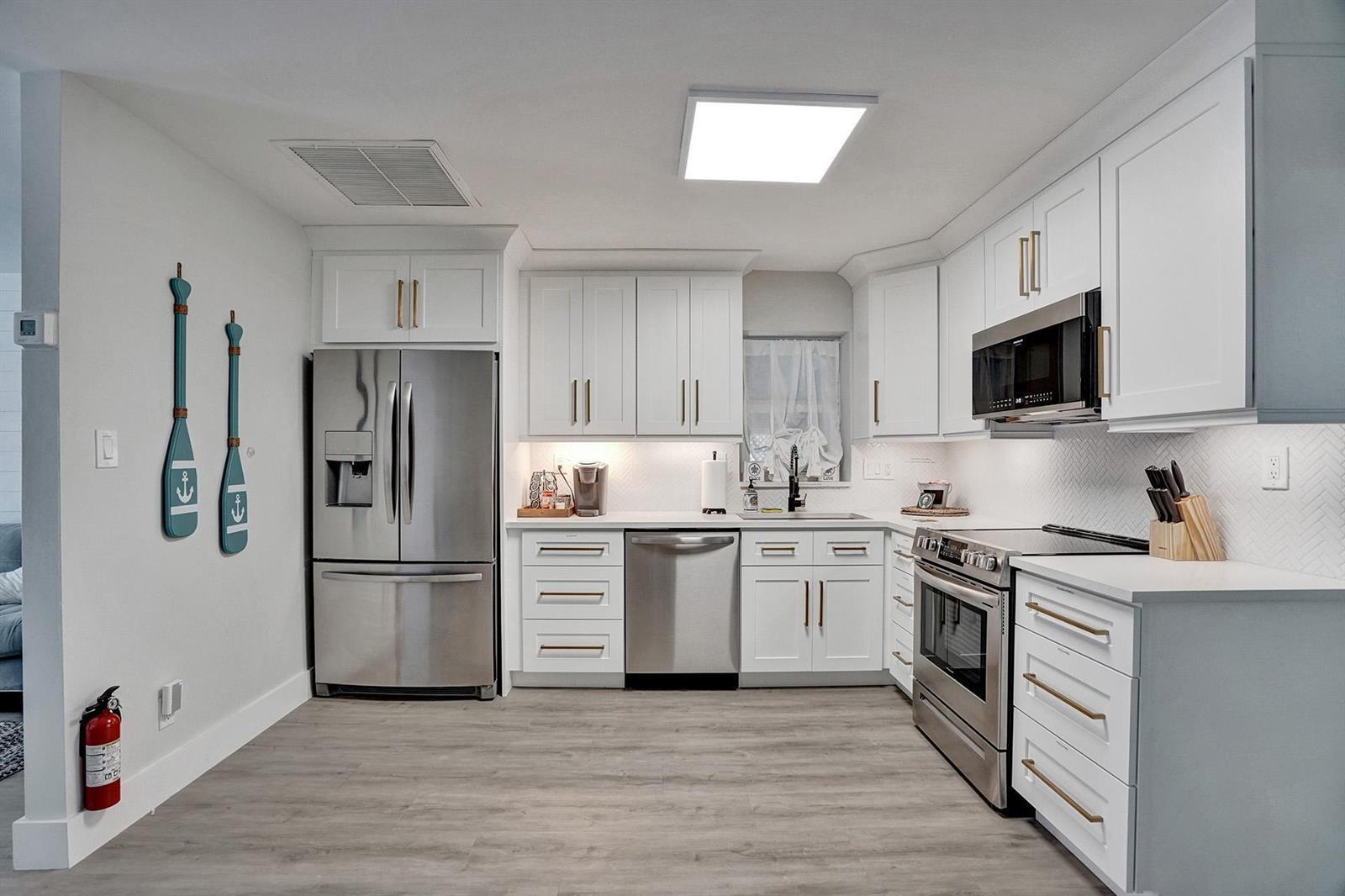 A modern kitchen features white cabinets, stainless steel appliances, and light wood-look flooring — 1969 NE 5th Street # 2, Deerfield Beach FL 33441, DEERFIELD BEACH, FL