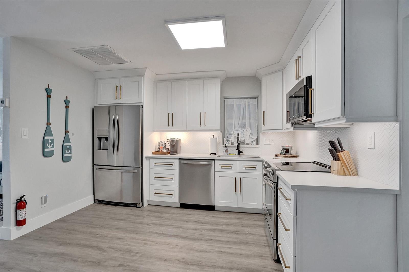 A modern kitchen features white cabinets, stainless steel appliances, and light wood-look flooring — 1969 NE 5th Street # 2, Deerfield Beach FL 33441, DEERFIELD BEACH, FL