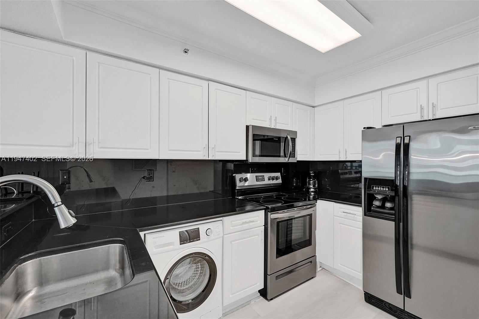 A kitchen features white cabinets, black countertops, stainless steel appliances, and an integrated washing machine — 2501 S Ocean Dr, Hollywood FL 33019, HOLLYWOOD, FL