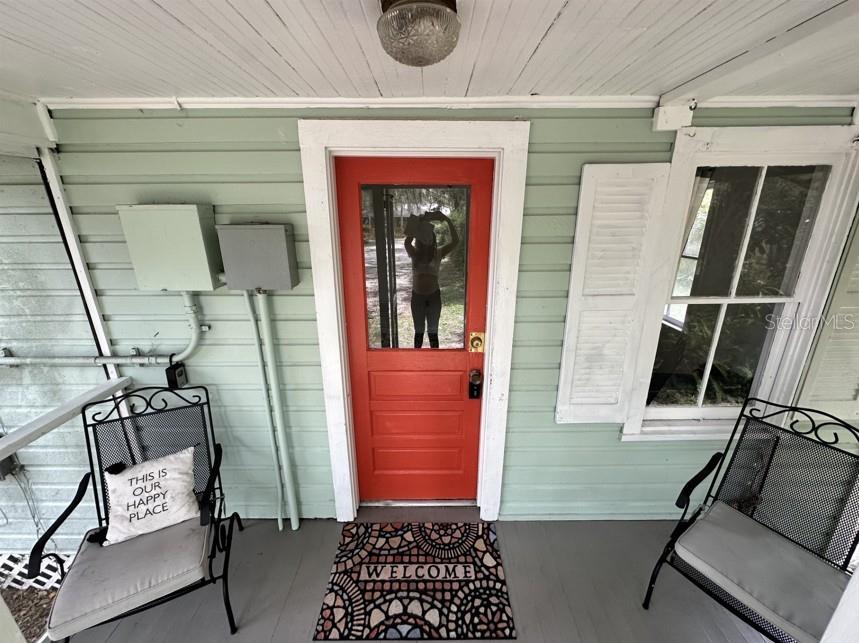A covered front porch features light green siding, a bright red door, and two chairs — 725 NE 5TH AVENUE, GAINESVILLE, FL