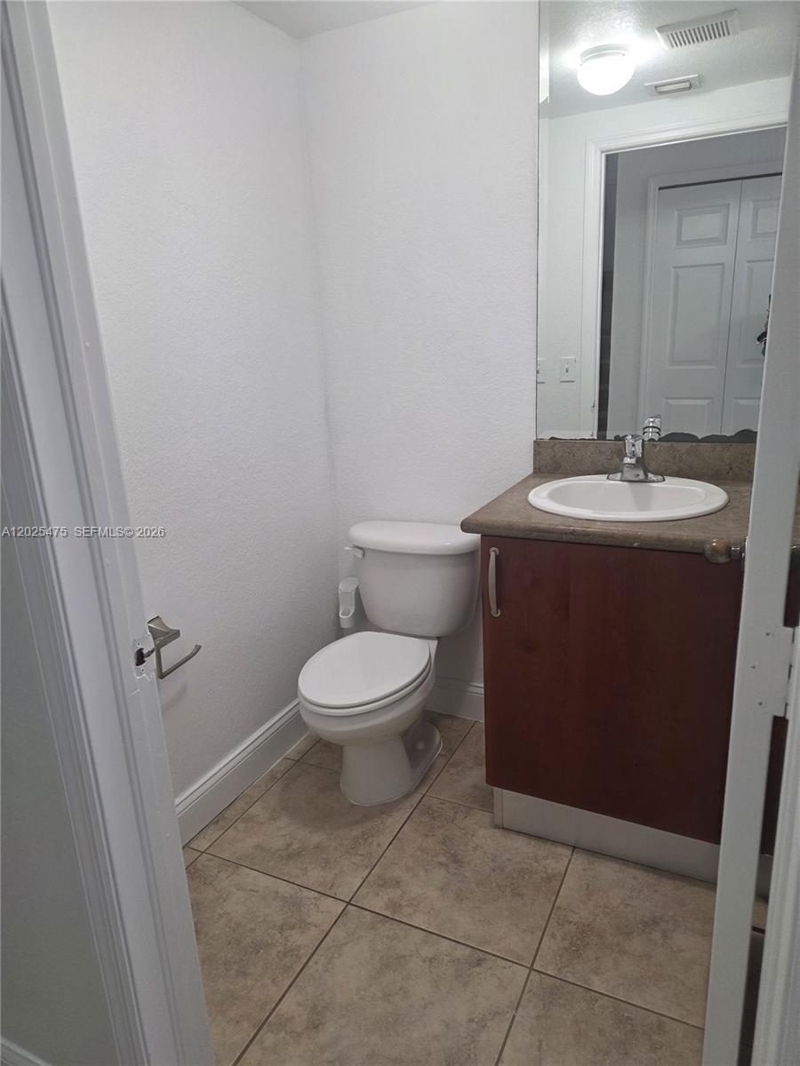 A small bathroom features a white toilet, a wood vanity with a sink, and tile flooring — 7477 NW 181, Hialeah FL 33015, HIALEAH, FL