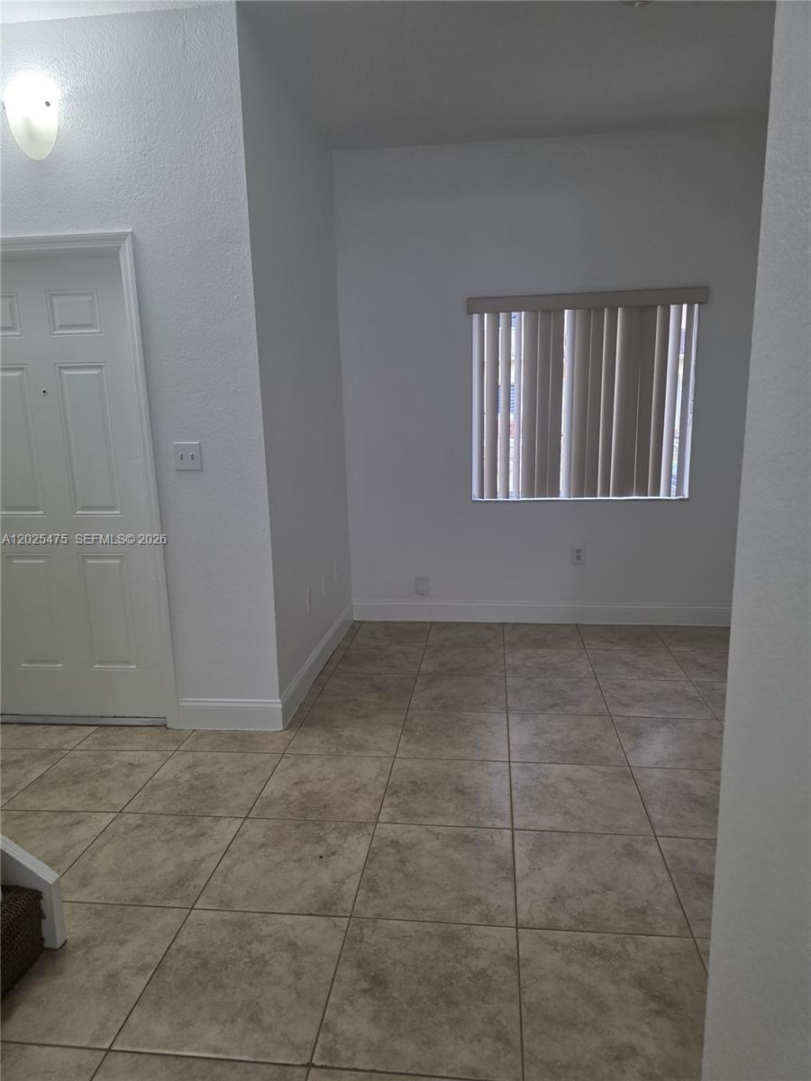 An empty room features white walls, tile flooring, a window with vertical blinds, and a door — 7477 NW 181, Hialeah FL 33015, HIALEAH, FL