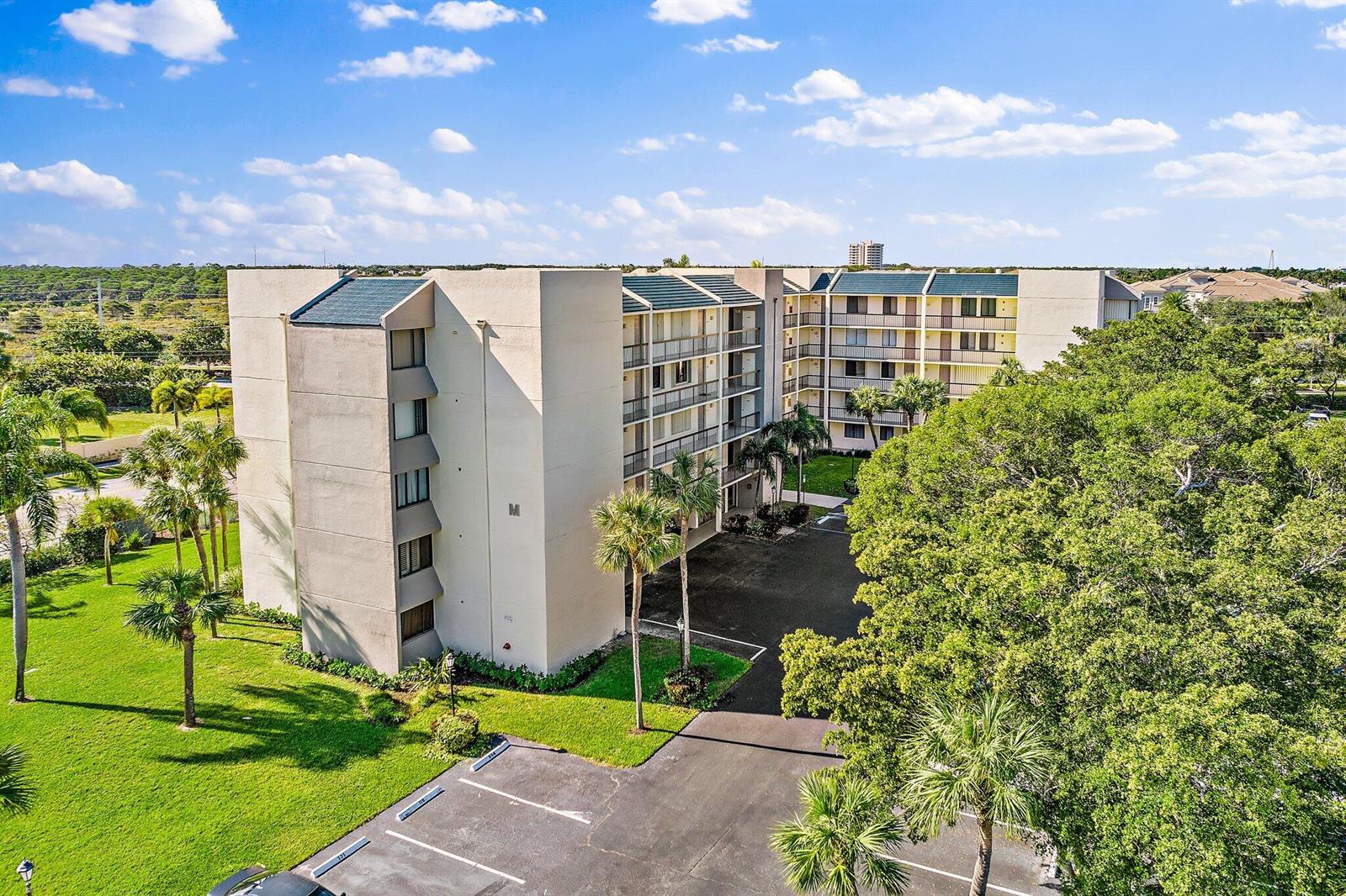 An aerial view of a multi-story apartment building with a parking lot and surrounding trees — 1605 S Us Highway 1 # 506, Jupiter FL 33477, JUPITER, FL