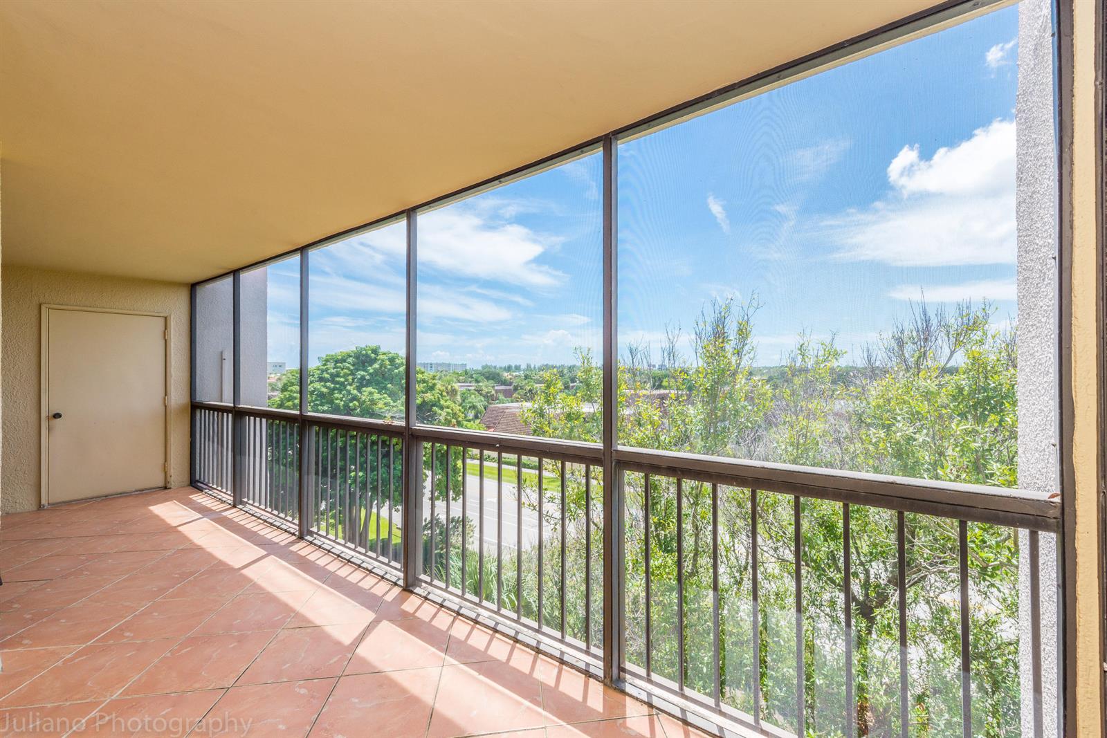 A screened-in balcony features tiled flooring, metal railings, and a view of trees and sky — 1605 S Us Highway 1 # 506, Jupiter FL 33477, JUPITER, FL