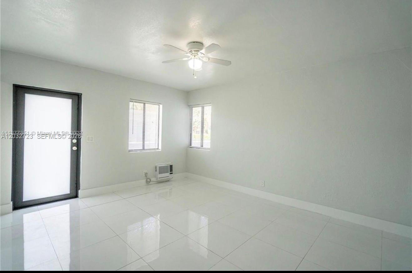 An empty room features white tile flooring, light gray walls, a ceiling fan, and windows — MIAMI BEACH, FL