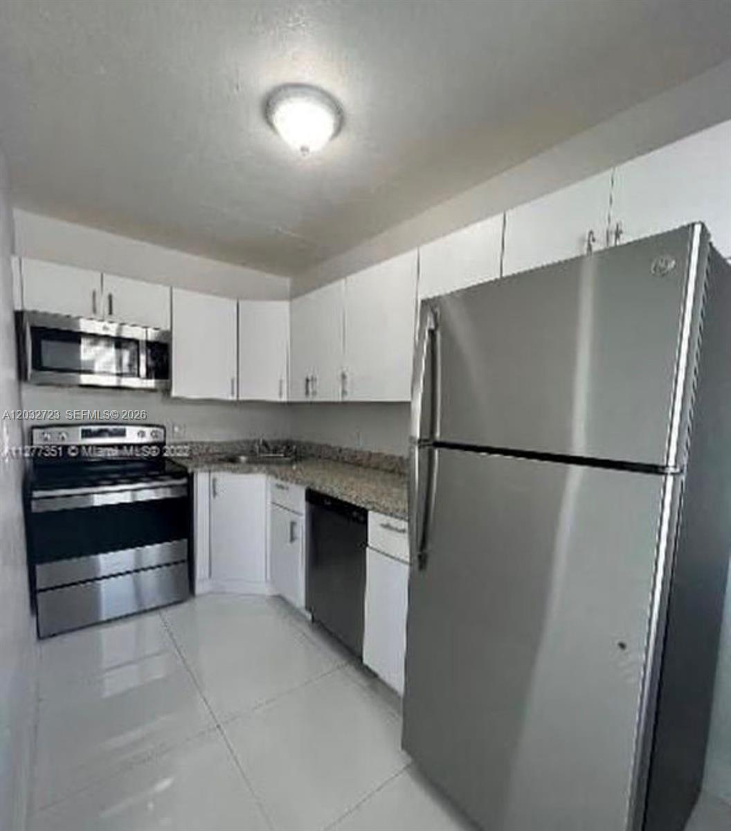 A kitchen features white cabinets, stainless steel appliances, granite countertops, and light tile flooring — MIAMI BEACH, FL
