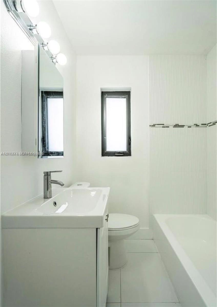 A modern bathroom features a white vanity, a toilet, and a bathtub with tile accents — MIAMI BEACH, FL
