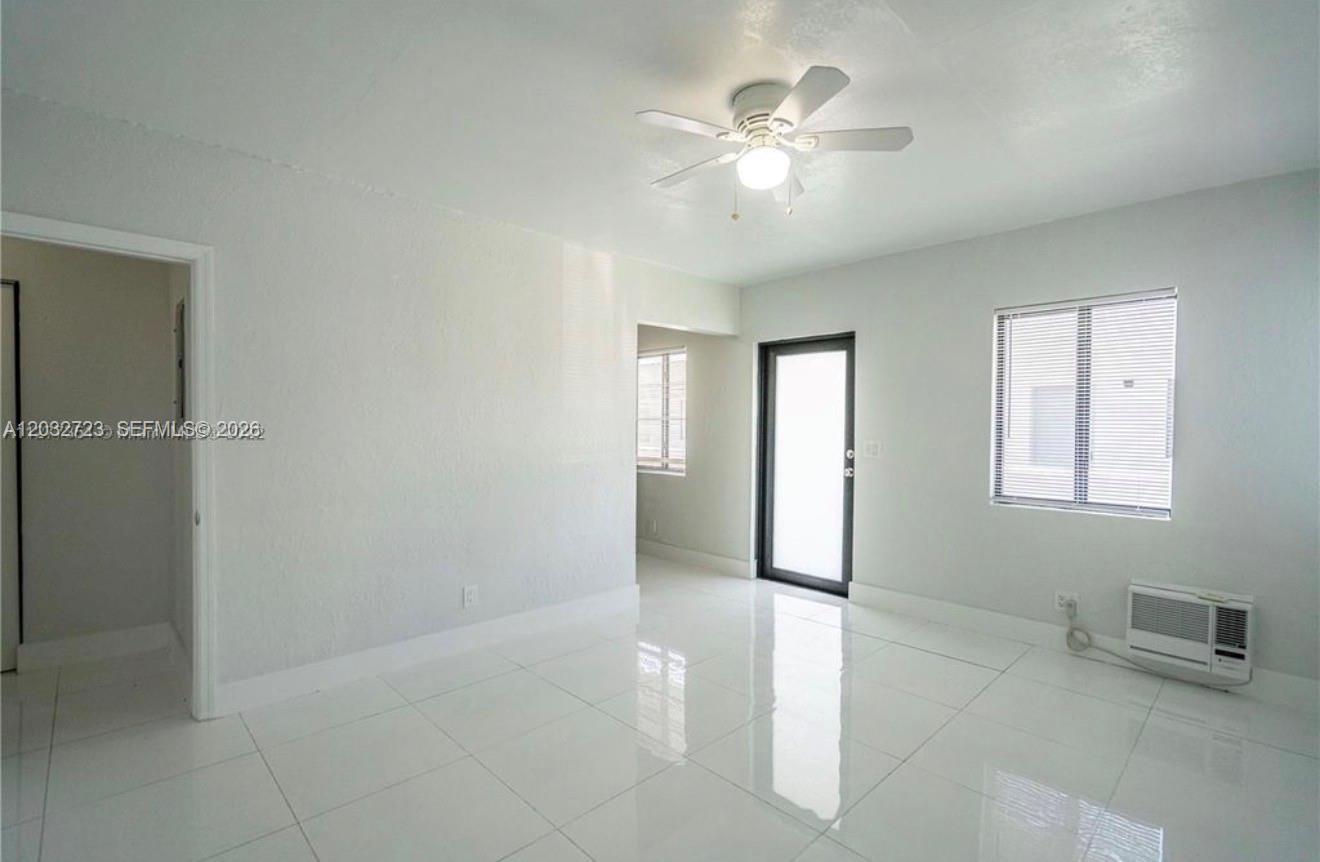 A bright, empty room features white tile flooring, a ceiling fan, and a window unit — MIAMI BEACH, FL