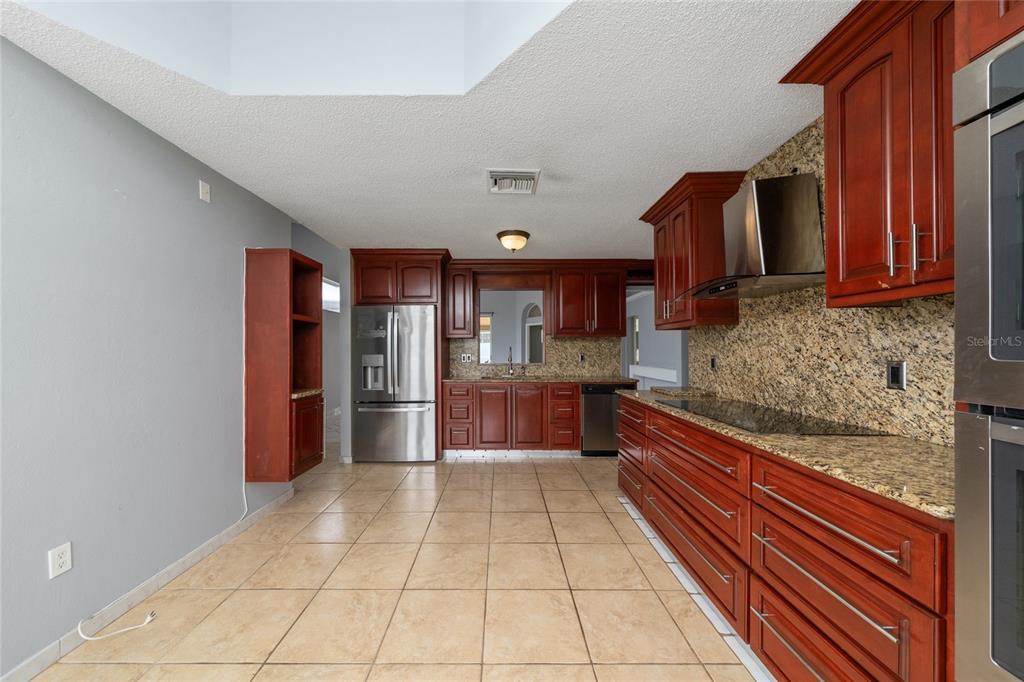 A kitchen with cherry wood cabinets, granite countertops, stainless steel appliances, and tiled flooring — 8810 KENSINGTON COURT, KISSIMMEE, FL