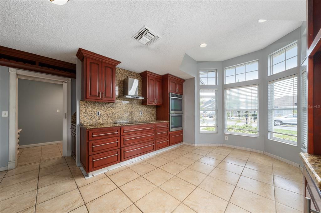 A kitchen features cherry wood cabinets, granite countertops, tile flooring, and a large bay window — 8810 KENSINGTON COURT, KISSIMMEE, FL