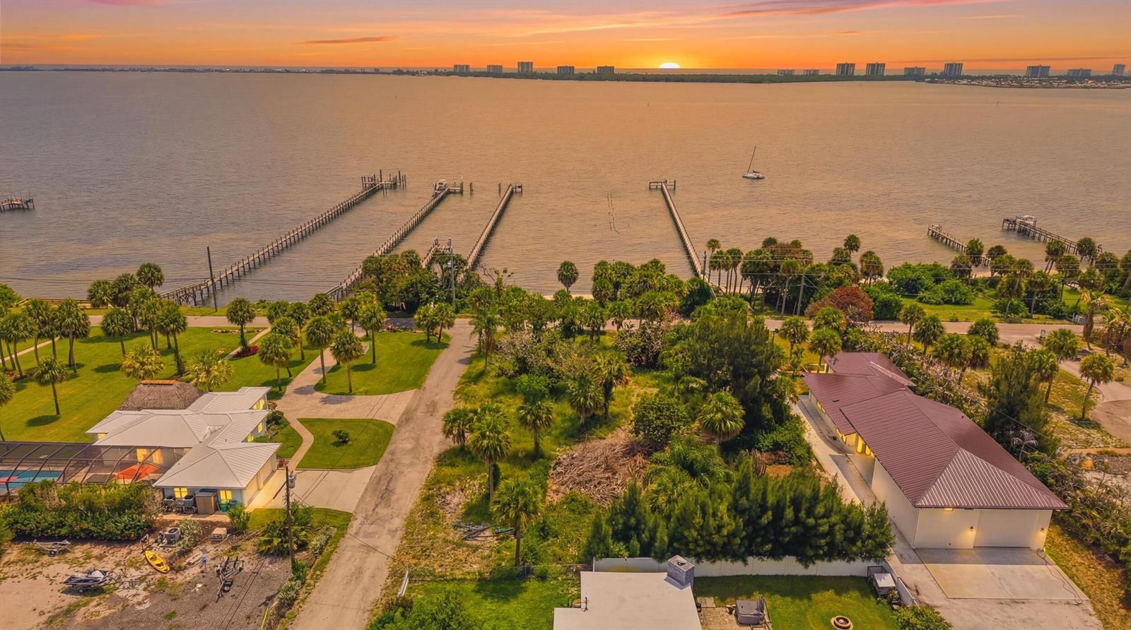 An aerial view shows two houses near a bay with multiple long wooden piers — 12349 S Indian River Drive, Jensen Beach FL 34957, JENSEN BEACH, FL