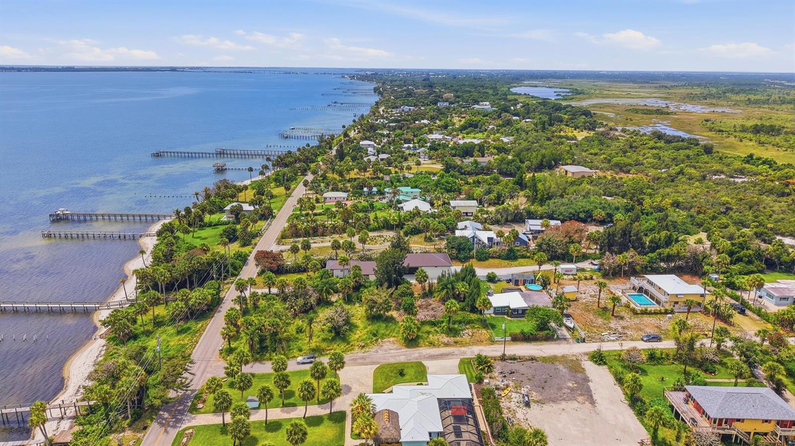 An aerial view shows a coastal neighborhood with houses, palm trees, and several long piers — 12349 S Indian River Drive, Jensen Beach FL 34957, JENSEN BEACH, FL