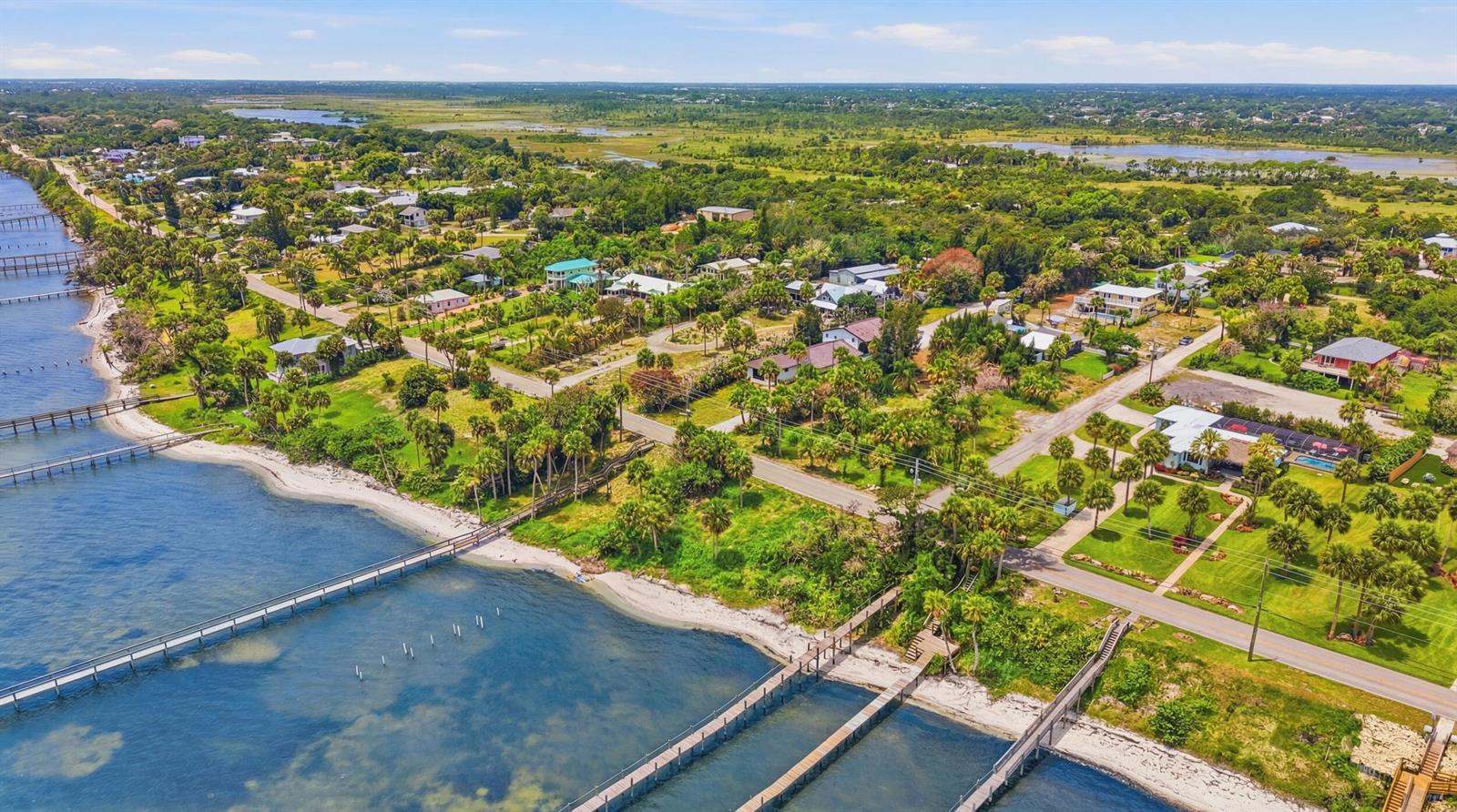 An aerial view shows a coastal neighborhood with multiple long wooden piers extending into water — 12349 S Indian River Drive, Jensen Beach FL 34957, JENSEN BEACH, FL