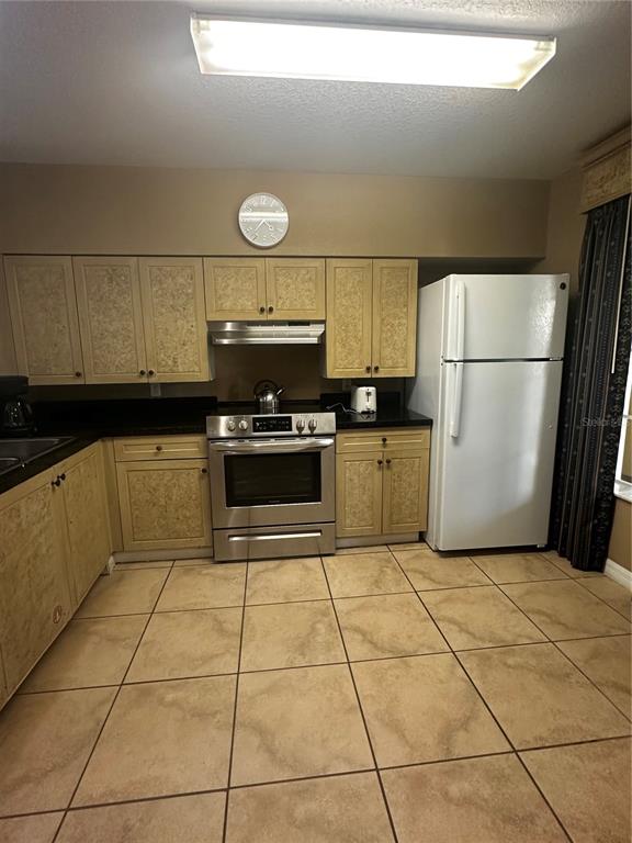 A kitchen features tan cabinets, black countertops, stainless steel appliances, and beige tile flooring — 8601 WORLDQUEST BOULEVARD UNIT 3-303, ORLANDO, FL