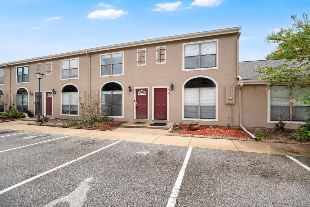 A two-story townhouse exterior with a tan stucco facade, red doors, and a parking lot — 611 CASA PARK A COURT, WINTER SPRINGS, FL