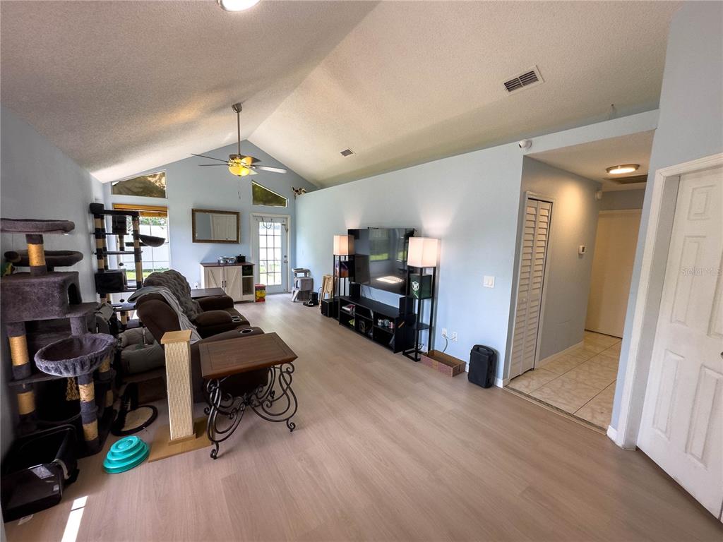 A living room features vaulted ceilings, light wood-look flooring, a ceiling fan, and a television — 9901 ALOMA BEND LANE, OVIEDO, FL