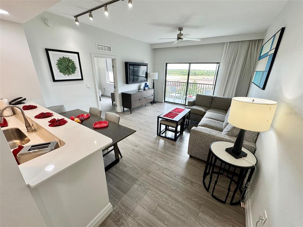 An open-concept living and dining area features light wood flooring, a kitchen island, and balcony access — 14501 GROVE RESORT AVENUE UNIT 3630, WINTER GARDEN, FL