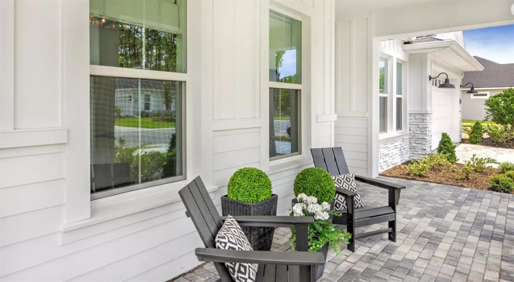A covered front porch features two black chairs, potted plants, and white siding — 54 BROADWATER ROAD, ORMOND BEACH, FL