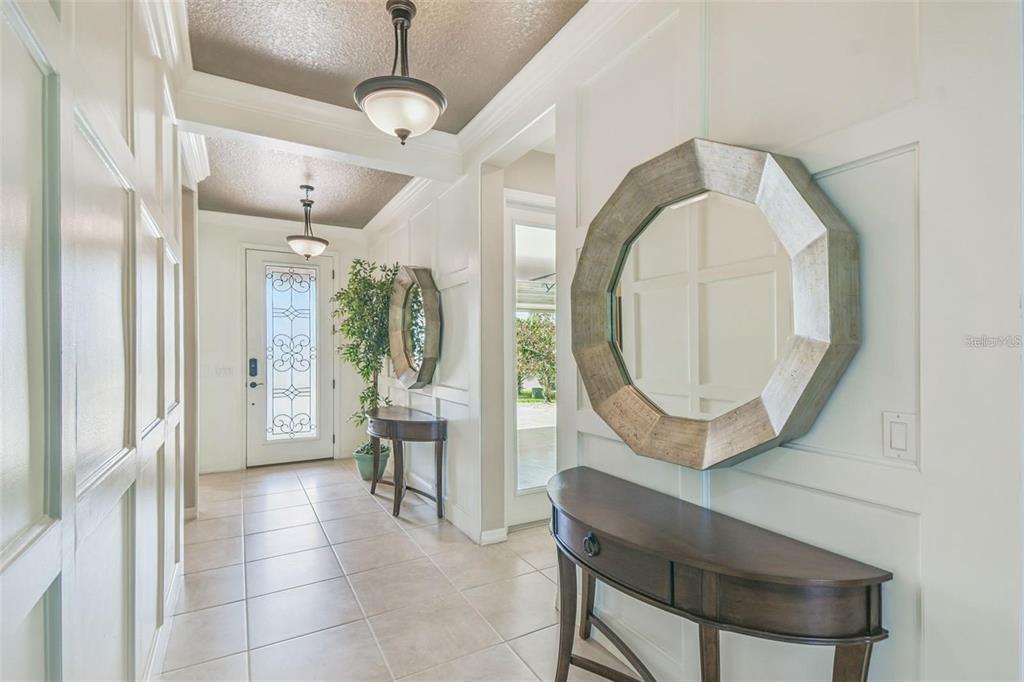 A bright entryway features tiled floors, white paneled walls, two console tables, and octagonal mirrors — 159 CASAVISTA DRIVE, KISSIMMEE, FL