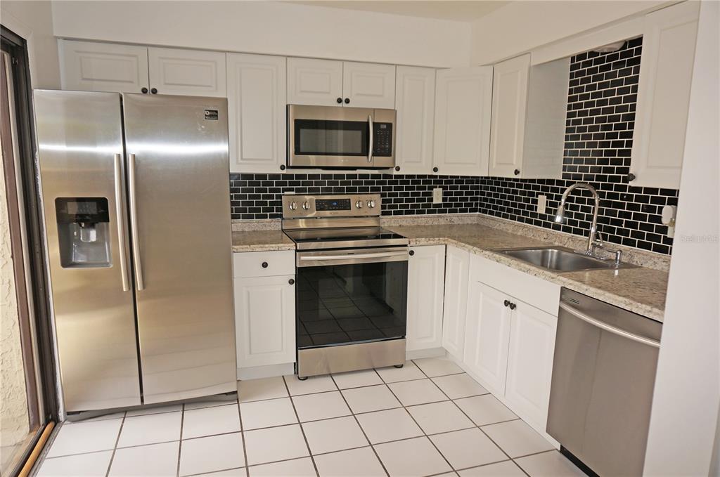 A kitchen with white cabinets, stainless steel appliances, granite countertops, and a black subway tile backsplash — 13100 S MCCALL ROAD UNIT 184, PORT CHARLOTTE, FL