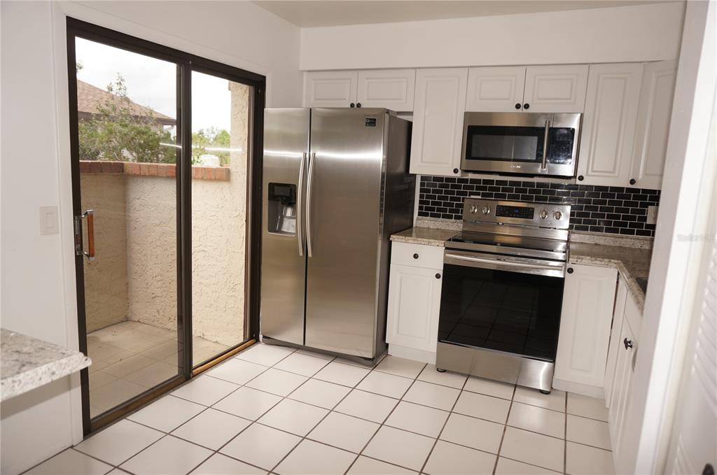 A kitchen with white cabinets, stainless steel appliances, black subway tile, and a sliding door — 13100 S MCCALL ROAD UNIT 184, PORT CHARLOTTE, FL