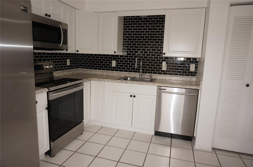 A kitchen features white cabinets, stainless steel appliances, black subway tile backsplash, and tiled flooring — 13100 S MCCALL ROAD UNIT 184, PORT CHARLOTTE, FL