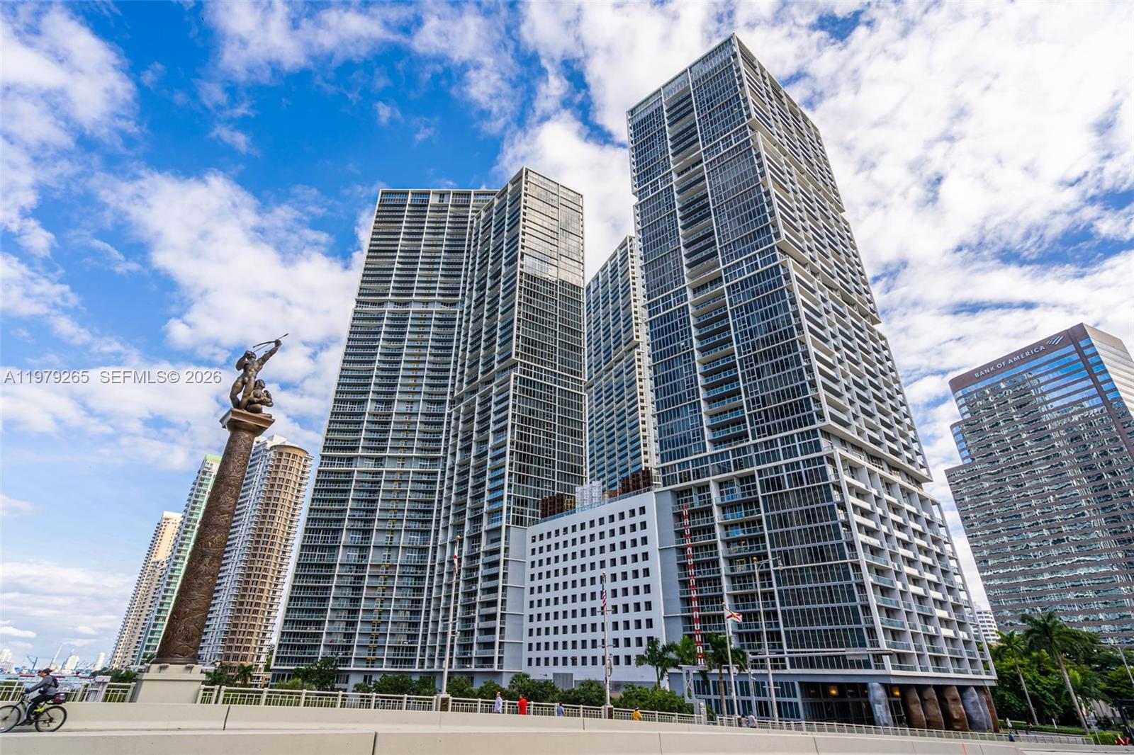 A low-angle view shows several modern glass skyscrapers and a prominent bronze statue — 495 Brickell Ave # 2909, Miami FL 33131, MIAMI, FL