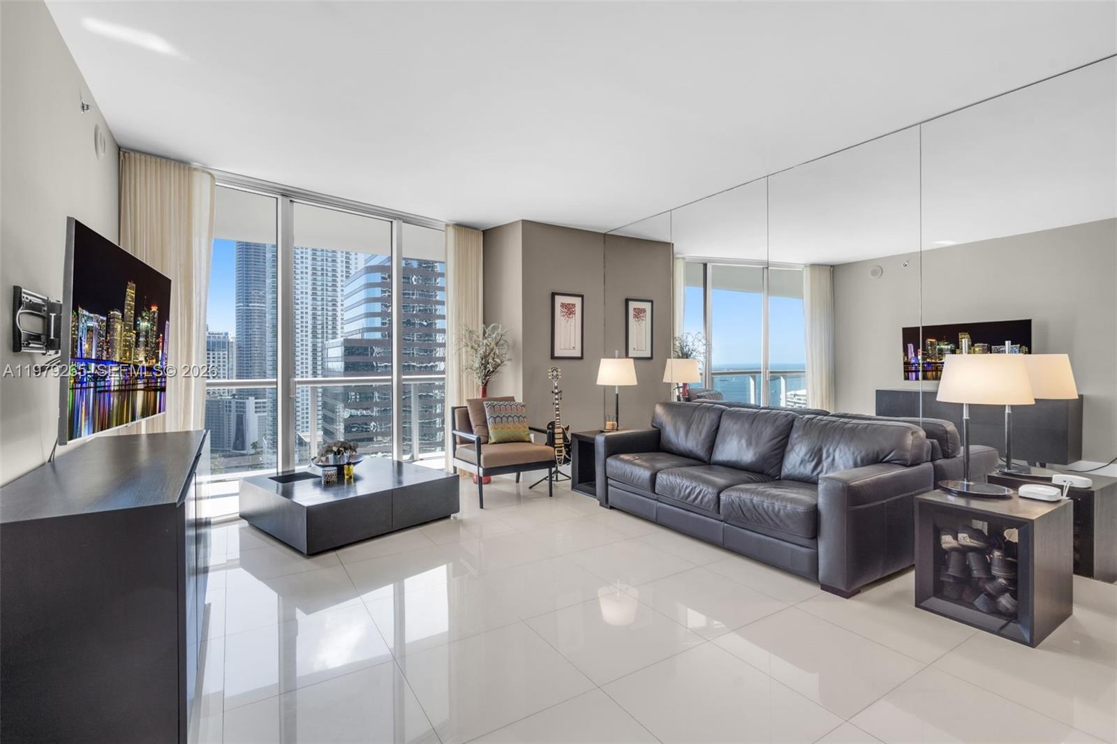 A modern living room features white tile floors, a leather sofa, and floor-to-ceiling windows — 495 Brickell Ave # 2909, Miami FL 33131, MIAMI, FL