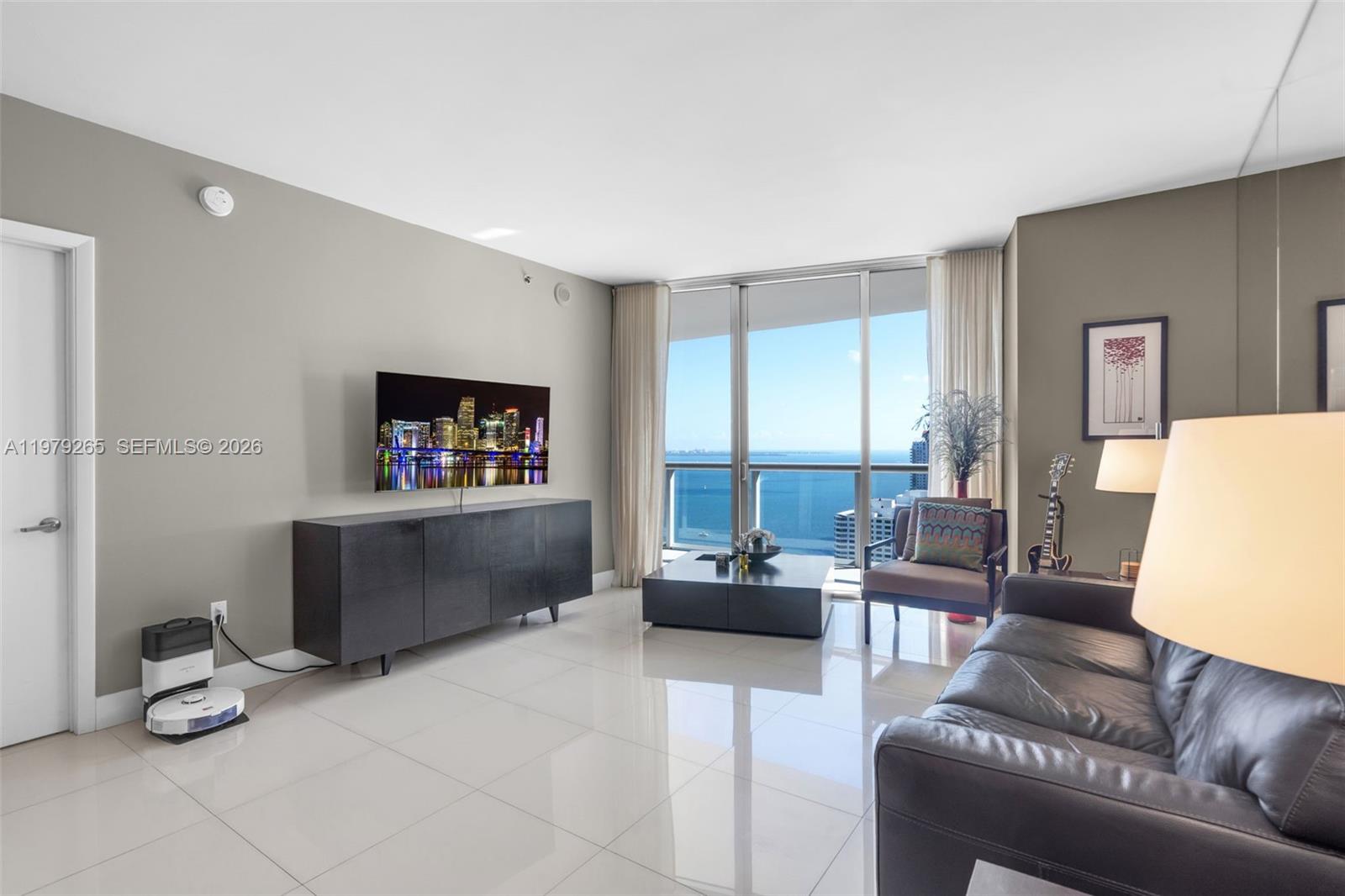 A modern living room features a dark media console, leather sofa, and floor-to-ceiling balcony windows — 495 Brickell Ave # 2909, Miami FL 33131, MIAMI, FL