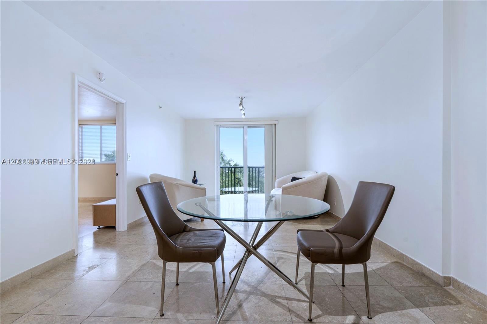 A dining area with a glass table and two chairs sits before a balcony door — 8888 Collins Ave # 314, Surfside FL 33154, SURFSIDE, FL