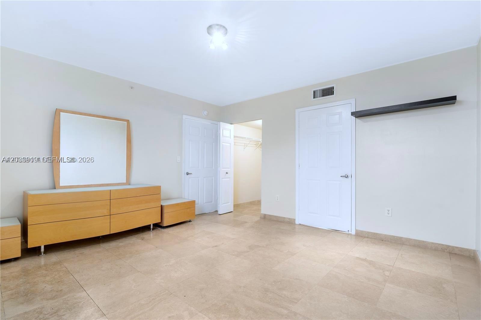 This bedroom features light-colored tile flooring, a wooden dresser with a mirror, and two doors — 8888 Collins Ave # 314, Surfside FL 33154, SURFSIDE, FL
