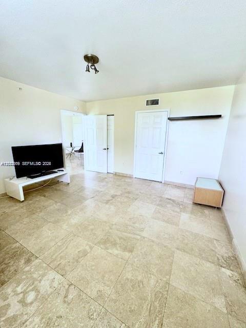 A living room with light-colored tile flooring, a television on a stand, and white doors — 8888 Collins Ave # 314, Surfside FL 33154, SURFSIDE, FL