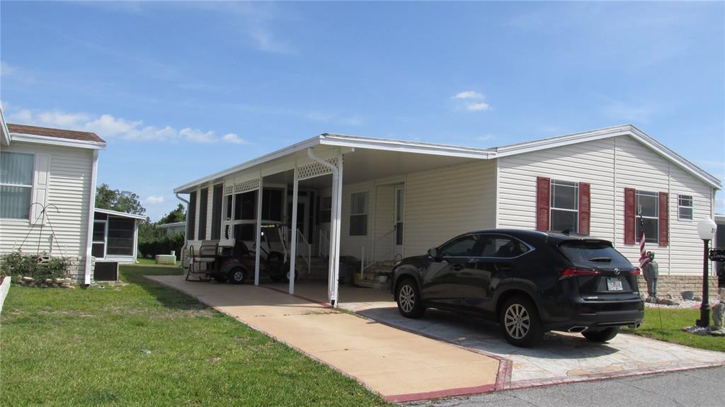 A single-story manufactured home with a carport, a black SUV, and a screened-in porch area — 212 YORK COTTAGE DRIVE, HAINES CITY, FL