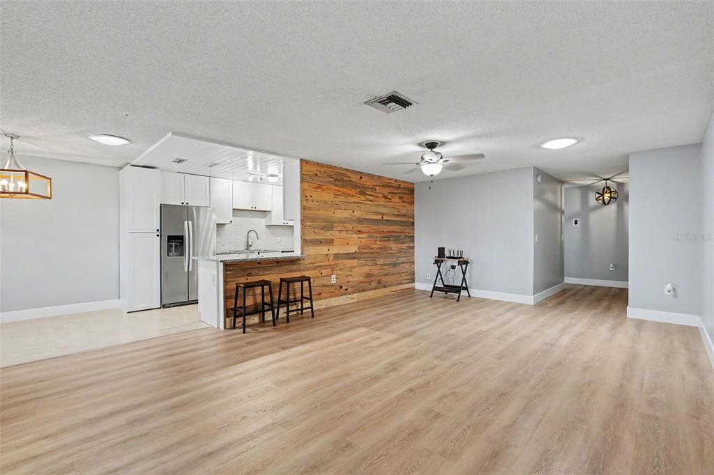 An open-concept living area features light wood flooring, a wood-paneled accent wall, and a kitchen — 1208 HIGHLAND AVENUE SE UNIT 121, LARGO, FL