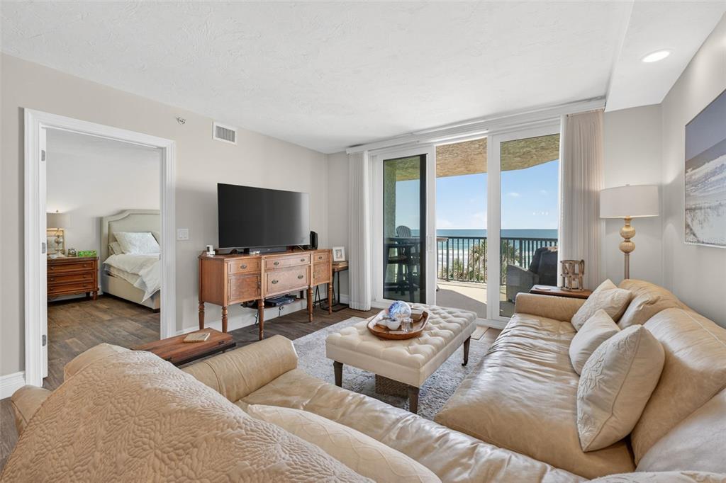 A living room features a leather sofa, tufted ottoman, and sliding doors opening to a balcony — 4631 S ATLANTIC AVENUE UNIT 8202, PORT ORANGE, FL