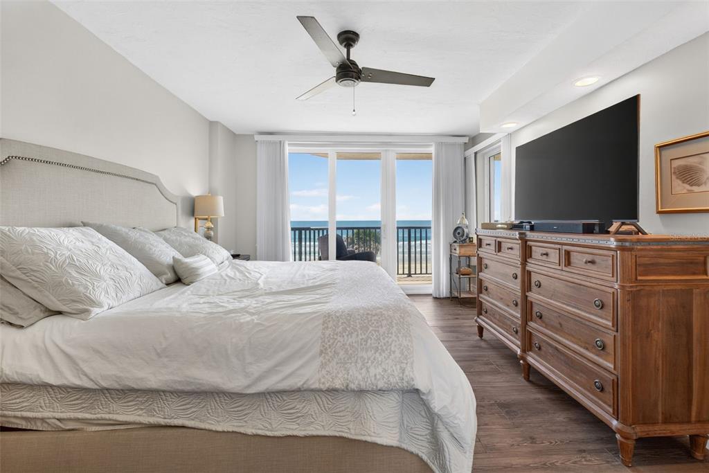 A bedroom features a large bed, a wooden dresser with a television, and a balcony view — 4631 S ATLANTIC AVENUE UNIT 8202, PORT ORANGE, FL
