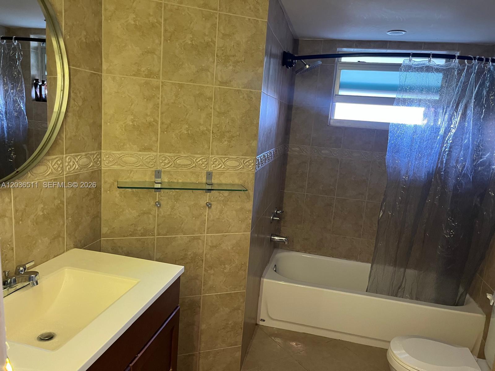 A bathroom features a vanity with a sink, a glass shelf, and a shower-tub combo — 1770 NE 191st St # 1, Miami FL 33179, MIAMI, FL