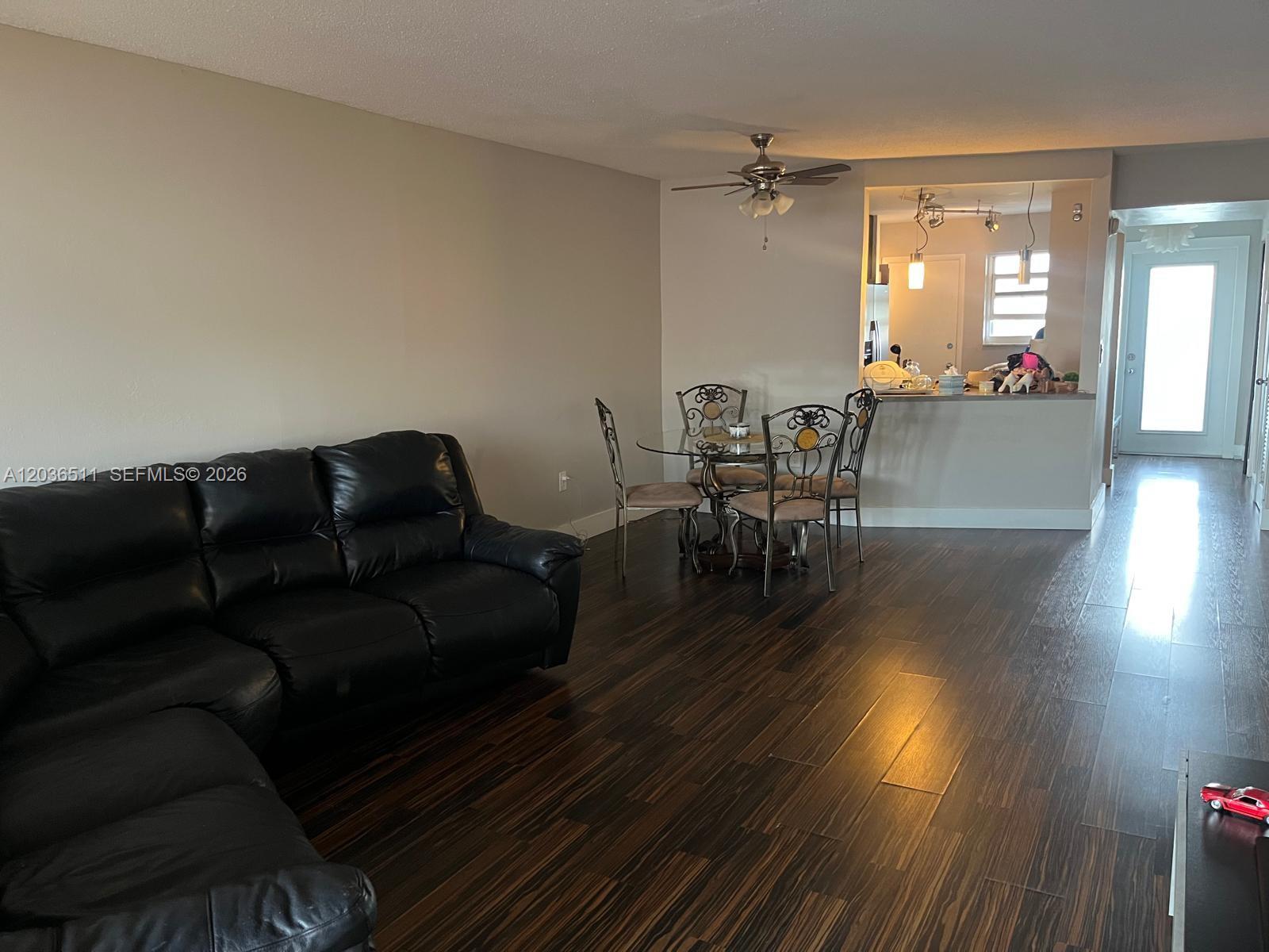 A living room with dark wood-look flooring, a black leather sofa, and a dining area — 1770 NE 191st St # 1, Miami FL 33179, MIAMI, FL
