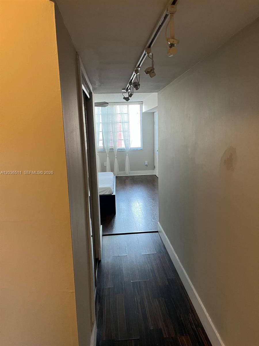 A narrow hallway with dark wood flooring leads to a bedroom with a window — 1770 NE 191st St # 1, Miami FL 33179, MIAMI, FL