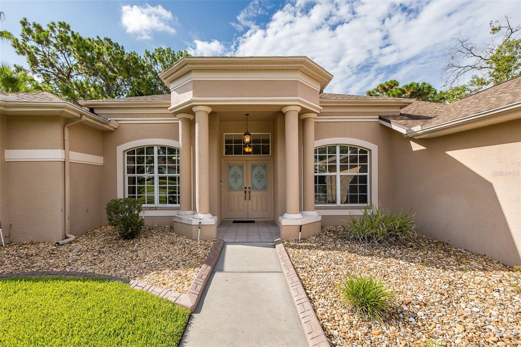 The exterior of a beige house features a covered entryway with four columns and double doors — 5436 CHAMPIONSHIP CUP LANE, SPRING HILL, FL